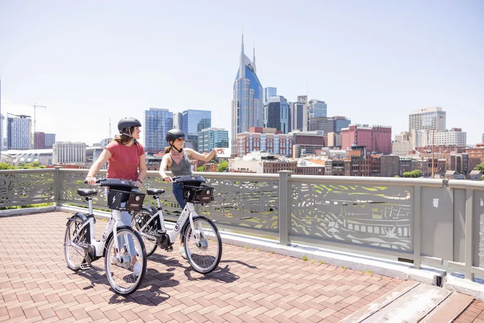 Two people on Nashville BCycle bike share wearing helmets loking out over railing at downtown skyline.